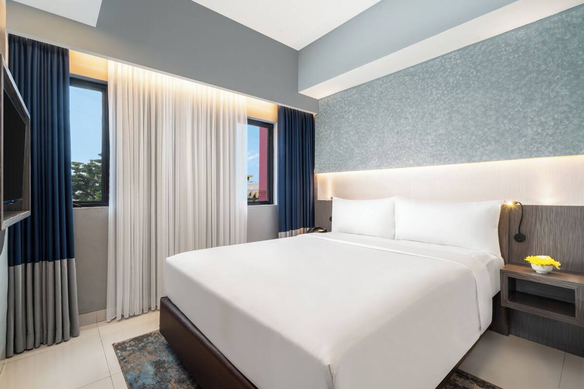 Hotelkamer met een groot bed, nachtkastje met lamp, raam met gordijnen en uitzicht op het exterieur.