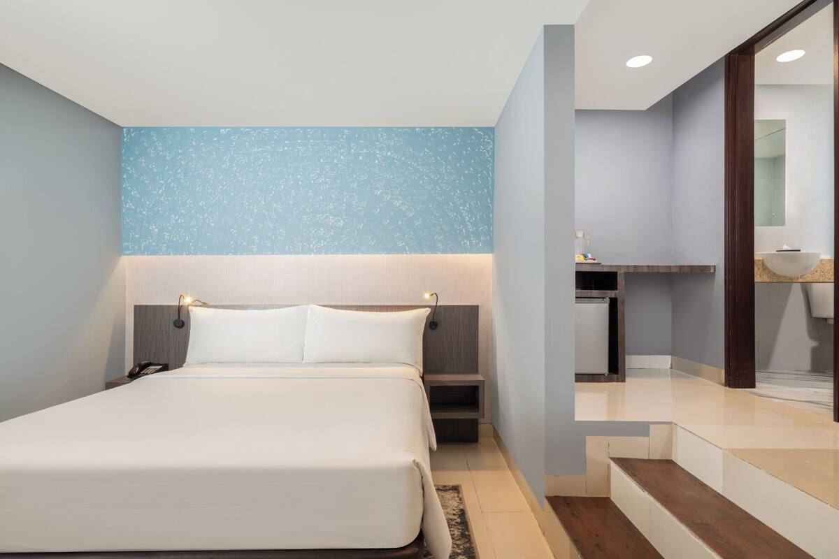 Een moderne hotelkamer met een groot bed, een nachtkastje, een klein bureau en een badkamer die door een open deur zichtbaar is.