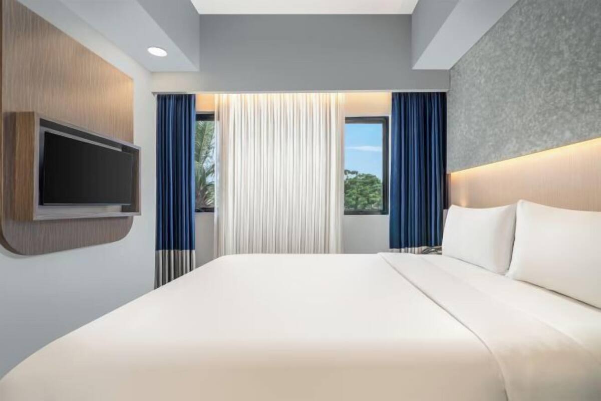 Een moderne hotelkamer met een groot bed, een flatscreen televisie aan de wand en uitzicht op groen.
