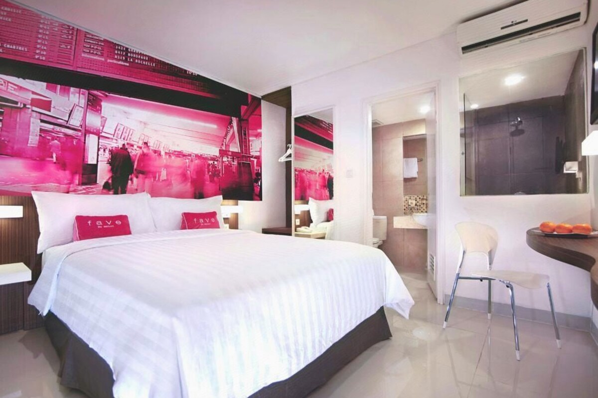 Une chambre d’hôtel avec un grand lit, un bureau avec une chaise, un miroir et un mur orné d’un motif abstrait rouge.