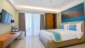 Habitación de hotel con una cama grande, televisor montado en la pared, escritorio con computadora y armario.