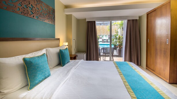 Habitación de hotel con una cama grande, vista a una piscina y un armario de madera.