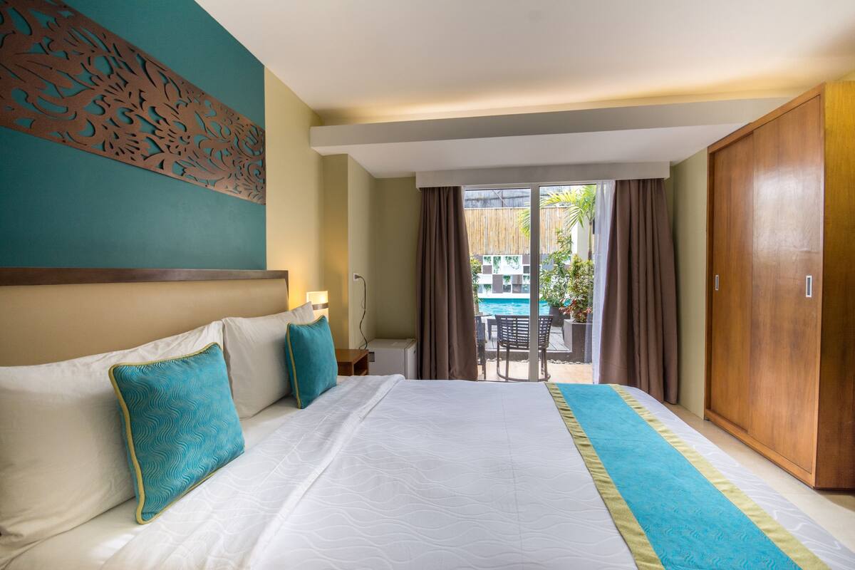 Habitación de hotel con una cama grande, vista a una piscina y un armario de madera.
