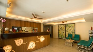 Un área de recepción con mostrador de madera, ventiladores de techo y mobiliario de mimbre.