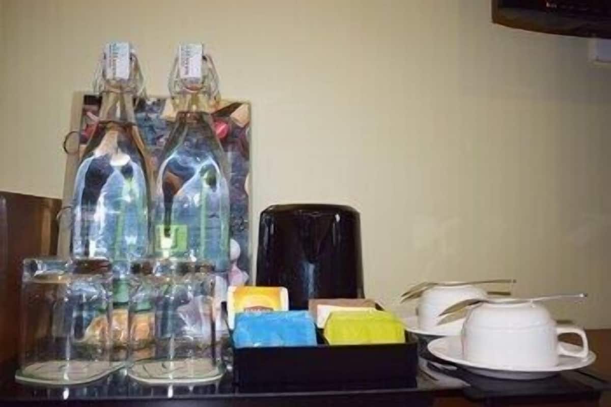 Una bandeja con una cafetera, dos botellas, una caja de pañuelos, una taza y un platito.
