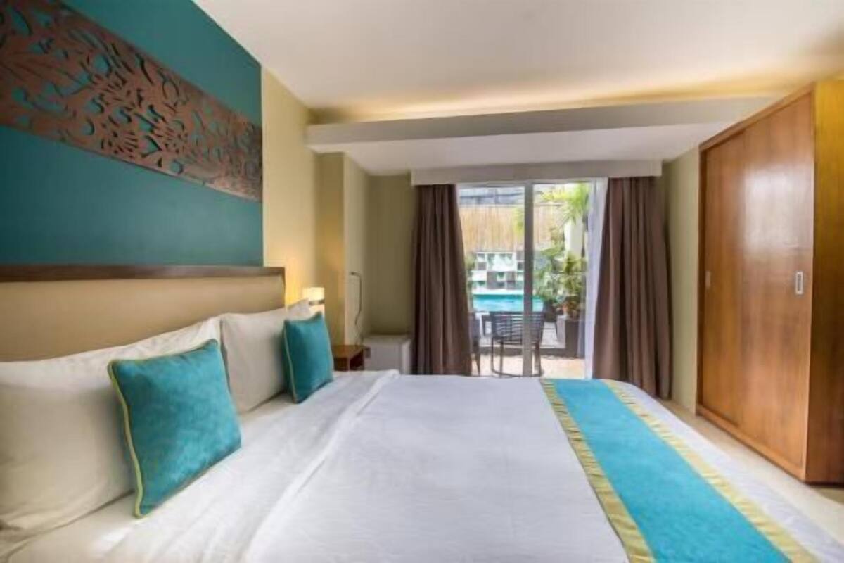Habitación de hotel con cama, vista a la piscina y puerta corrediza que da al exterior.