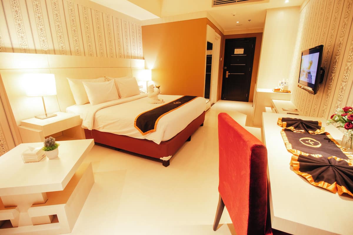 Une chambre d’hôtel comprenant un lit, des tables de chevet, un bureau, une chaise, une télévision et une plante décorative.