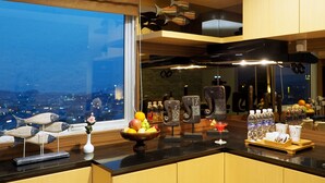 Een moderne keuken met stadszicht, voorzien van een houten aanrecht, decoratieve vissenbeeldjes, een fruitschaal en een bar met flessen en glazen.