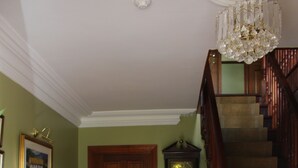Een trap met houten treden en een houten leuning, een houten bureau met een lamp, een stoel en een grote wandklok.
