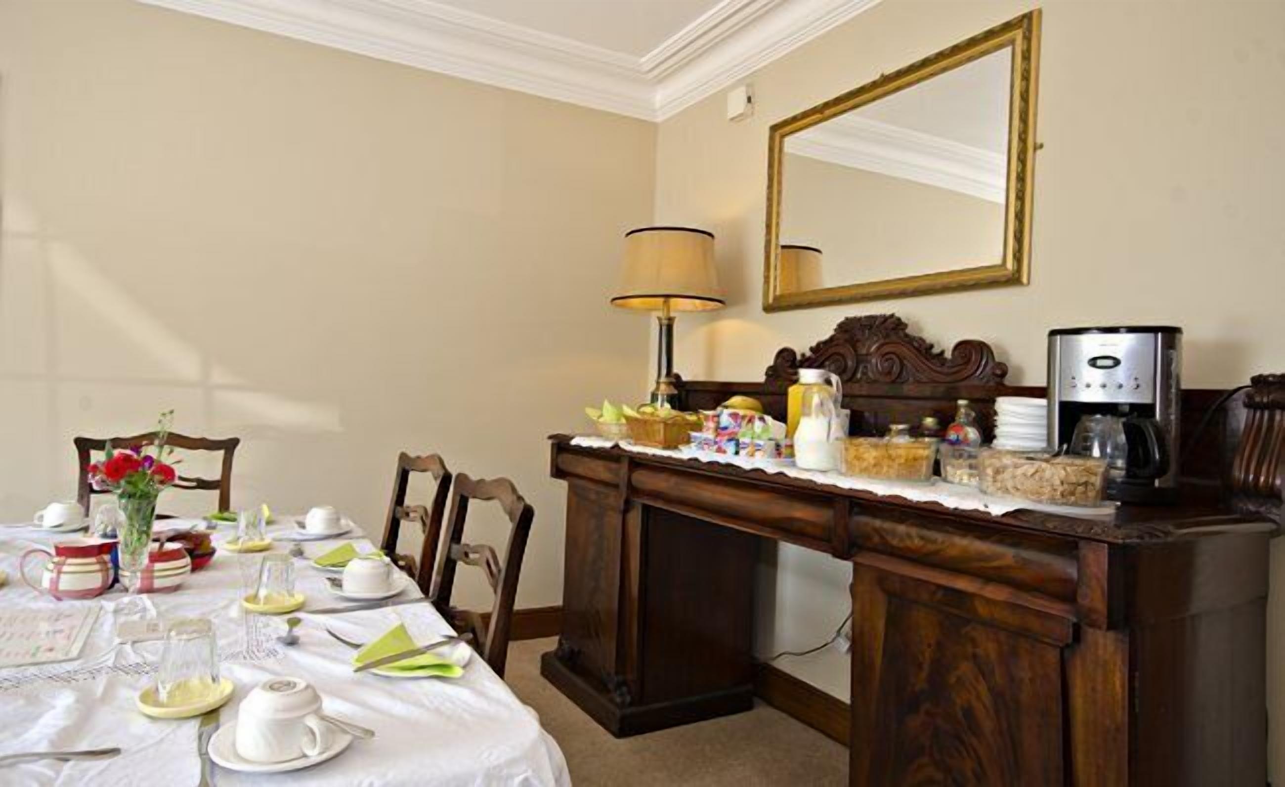 A dining area with a table set for breakfast, a coffee maker, and a mirror on the wall.