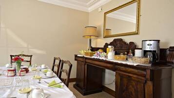 A dining area with a table set for breakfast, a coffee maker, and a mirror on the wall.