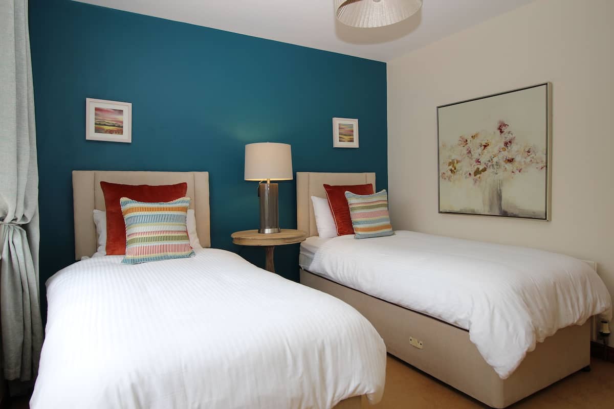 Een hotelkamer met twee bedden, een nachtkastje, een lamp en kunst aan de muren.