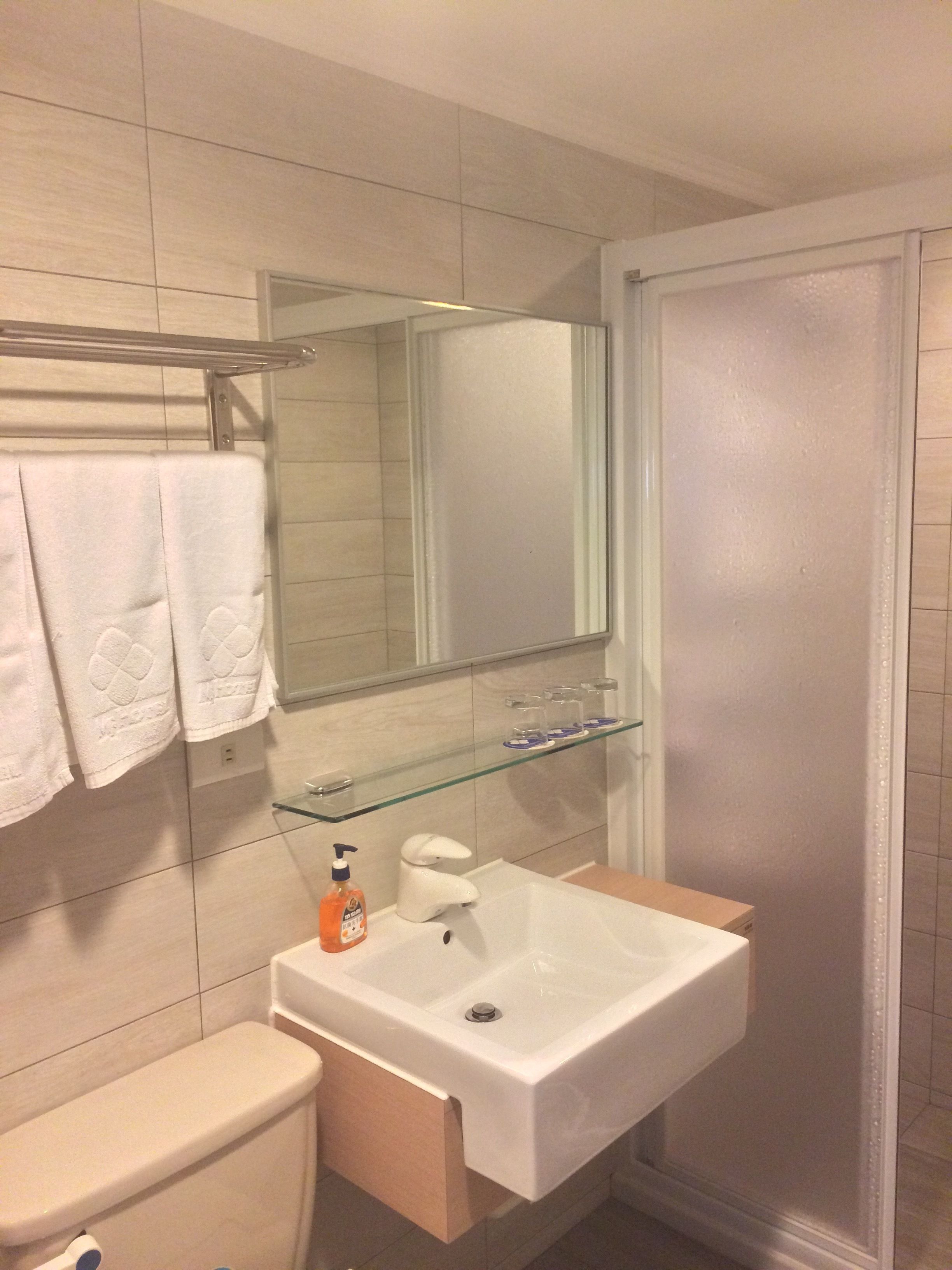 A modern bathroom with a white sink, a glass shelf above it, a toilet, and a glass shower enclosure.