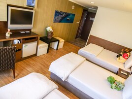 Habitación de hotel con dos camas, un escritorio con televisor, un refrigerador pequeño y una pared de madera con un cuadro.