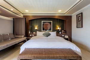 A hotel room with a large bed, a bench, and a small table with a lamp.