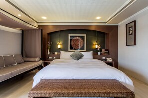 Una habitación de hotel con una cama grande, un banco y una mesita de noche con lámpara.
