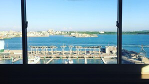 Vista desde el interior de un edificio hacia una marina con barcos y un paisaje urbano distante.