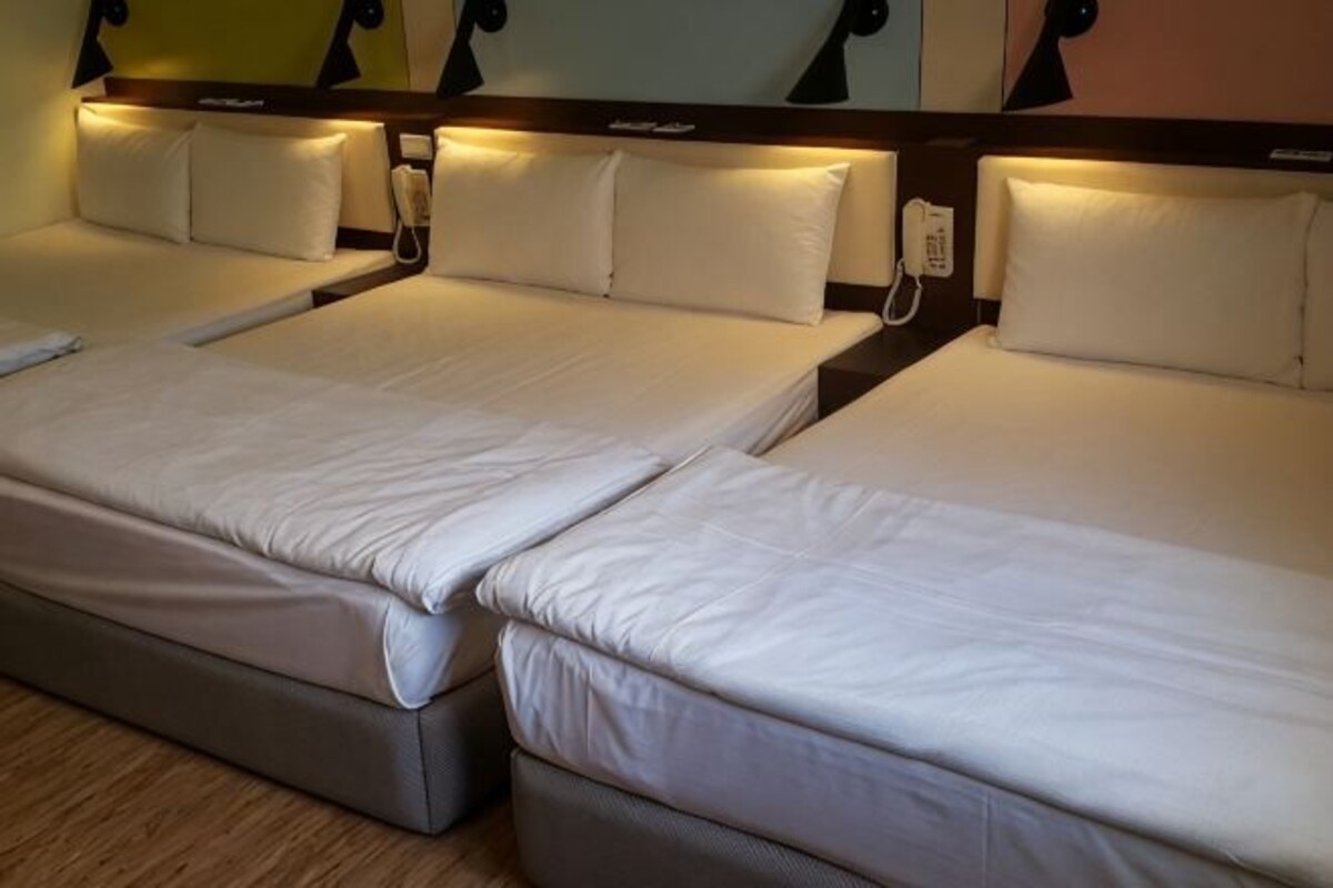 A hotel room with three single beds, each with a pillow and a headboard.