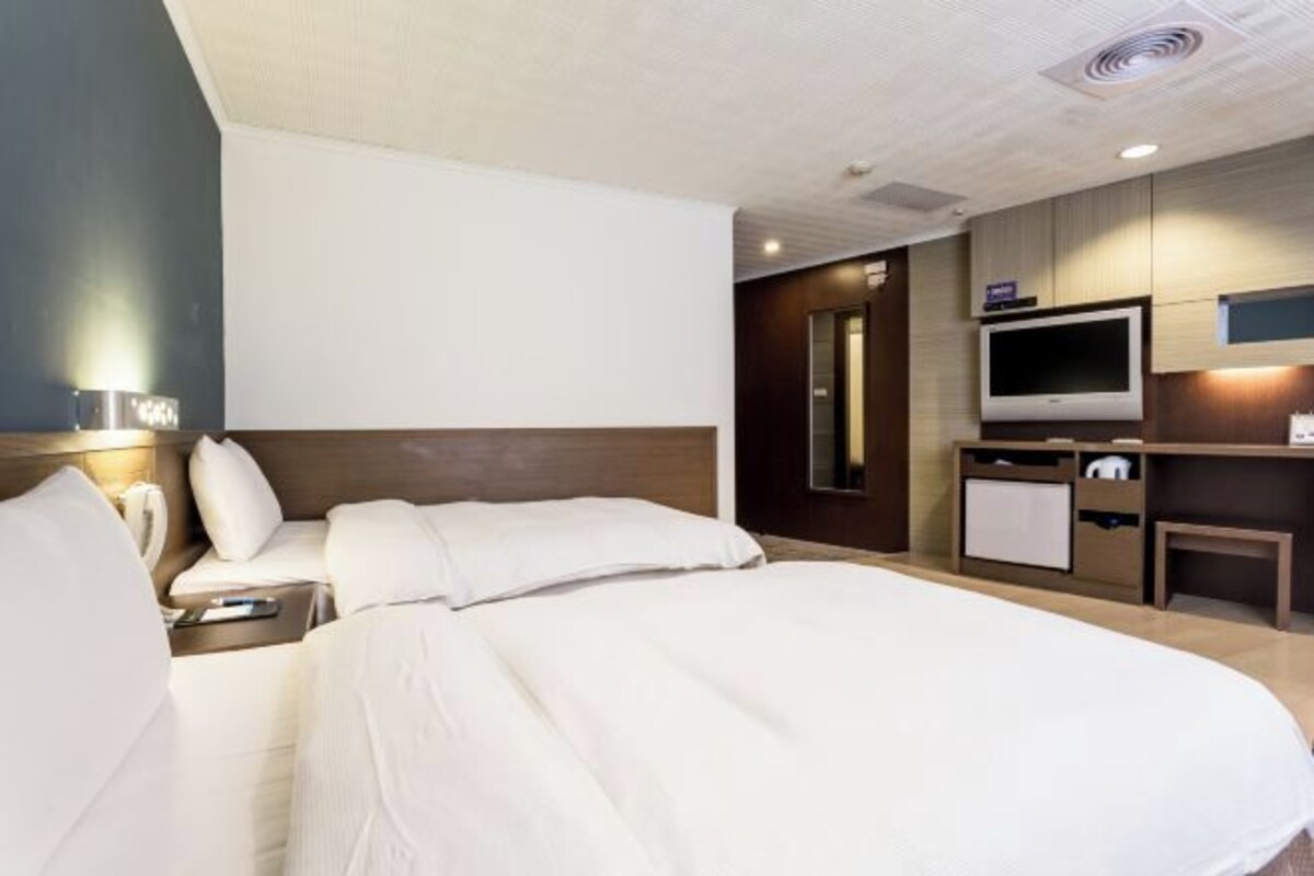 A hotel room with two beds, a TV, a desk, and a minibar.