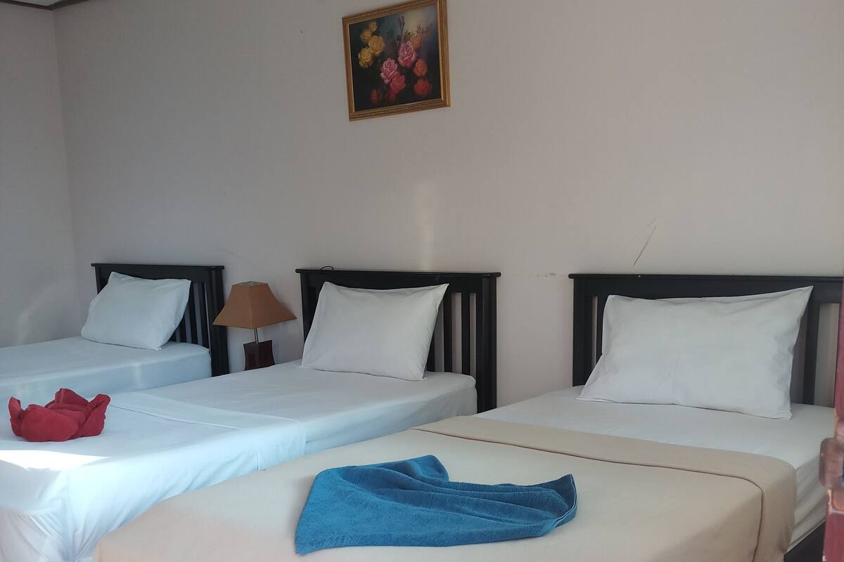 A hotel room with two beds, each with white bedding and a wooden headboard. There is a painting on the wall above the beds, and a lamp on the nightstand beside one of the beds.