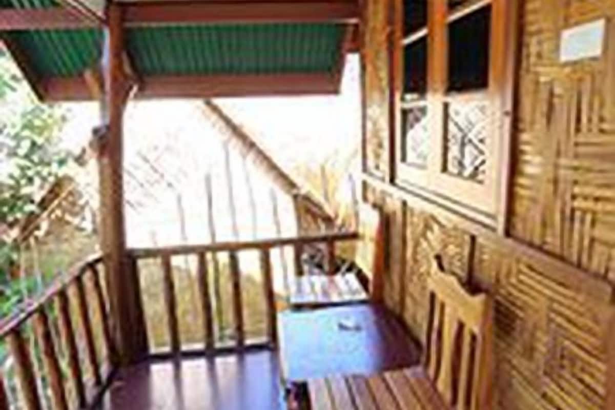 A wooden cabin with a balcony, a wooden bench, and a table.