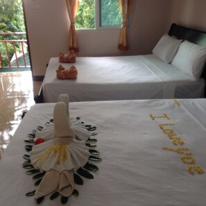 Quarto de hotel com duas camas, uma janela com cortinas e arranjo de toalhas sobre uma das camas.