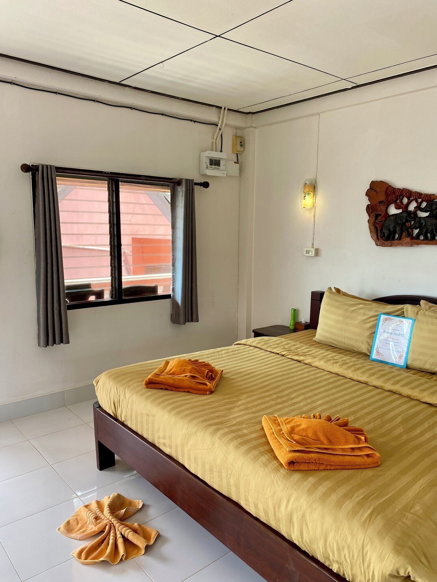 A hotel room with a bed, curtains, a wall-mounted light, and a decorative wall piece.