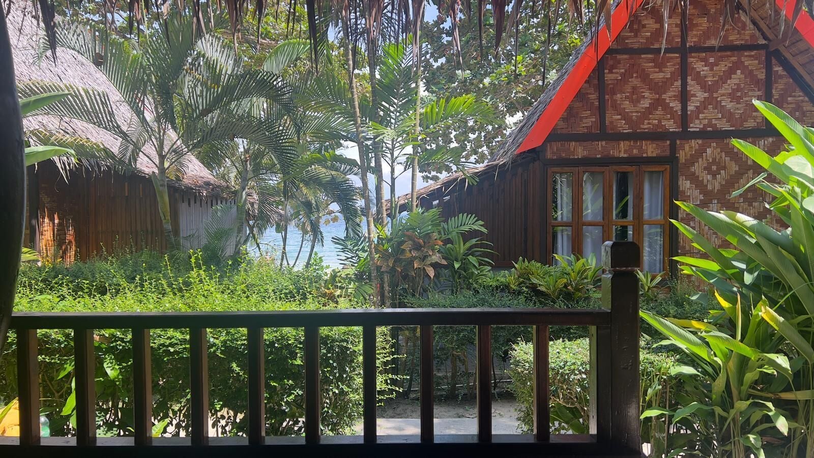 Una casa de madera tradicional con techo de paja, rodeada de exuberante vegetación tropical y vista al mar.