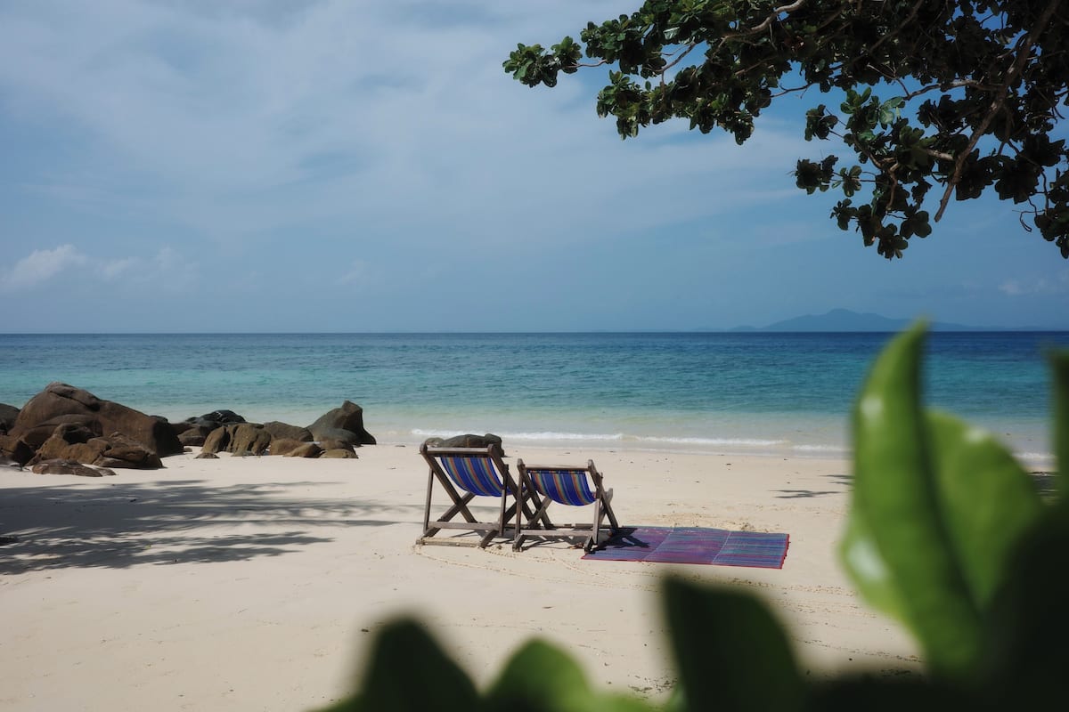 Une plage avec deux chaises longues en bois et un tapis coloré sur le sable.