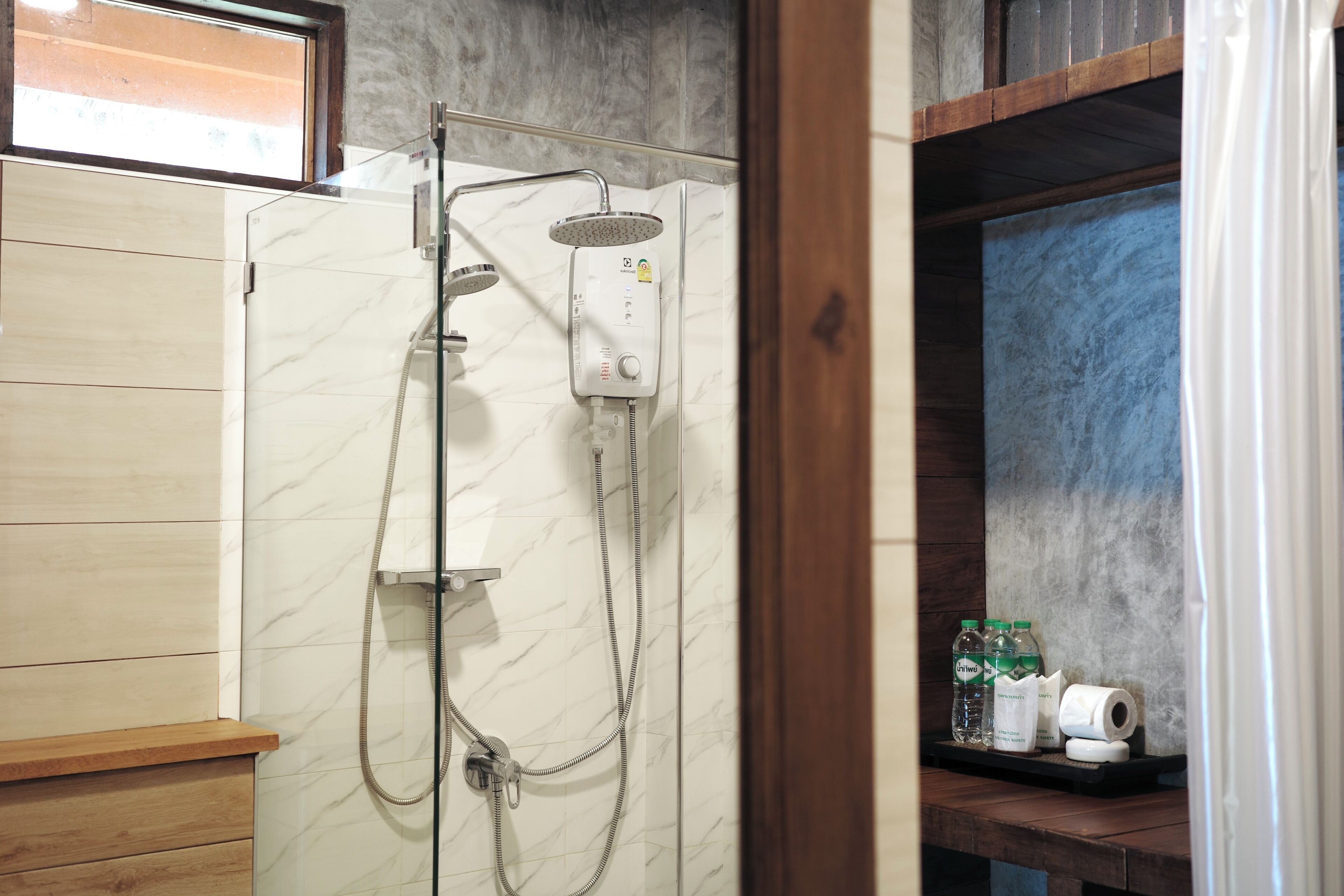 Douchecel met bedieningspaneel, handdouche en douchekop aan de muur. Er staan flessen en een rol toiletpapier op een plank.