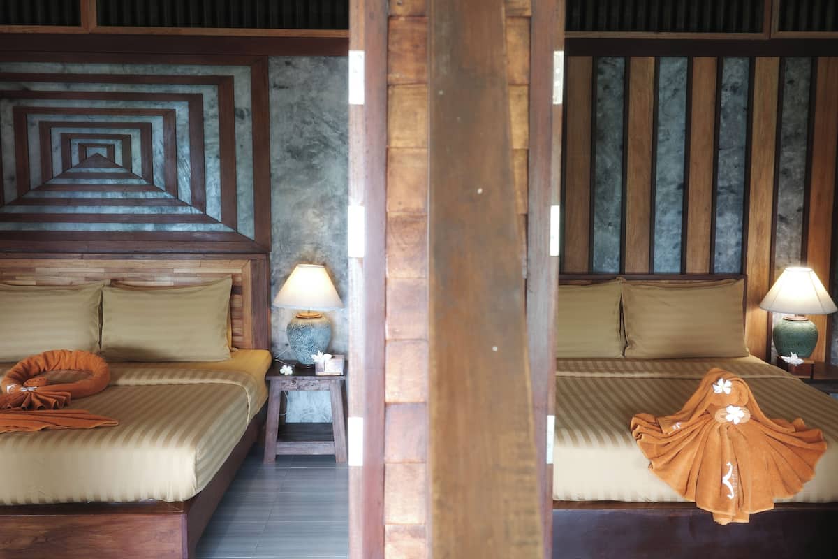 Une chambre d’hôtel avec deux lits, des têtes de lit en bois et une petite table de chevet avec une lampe.