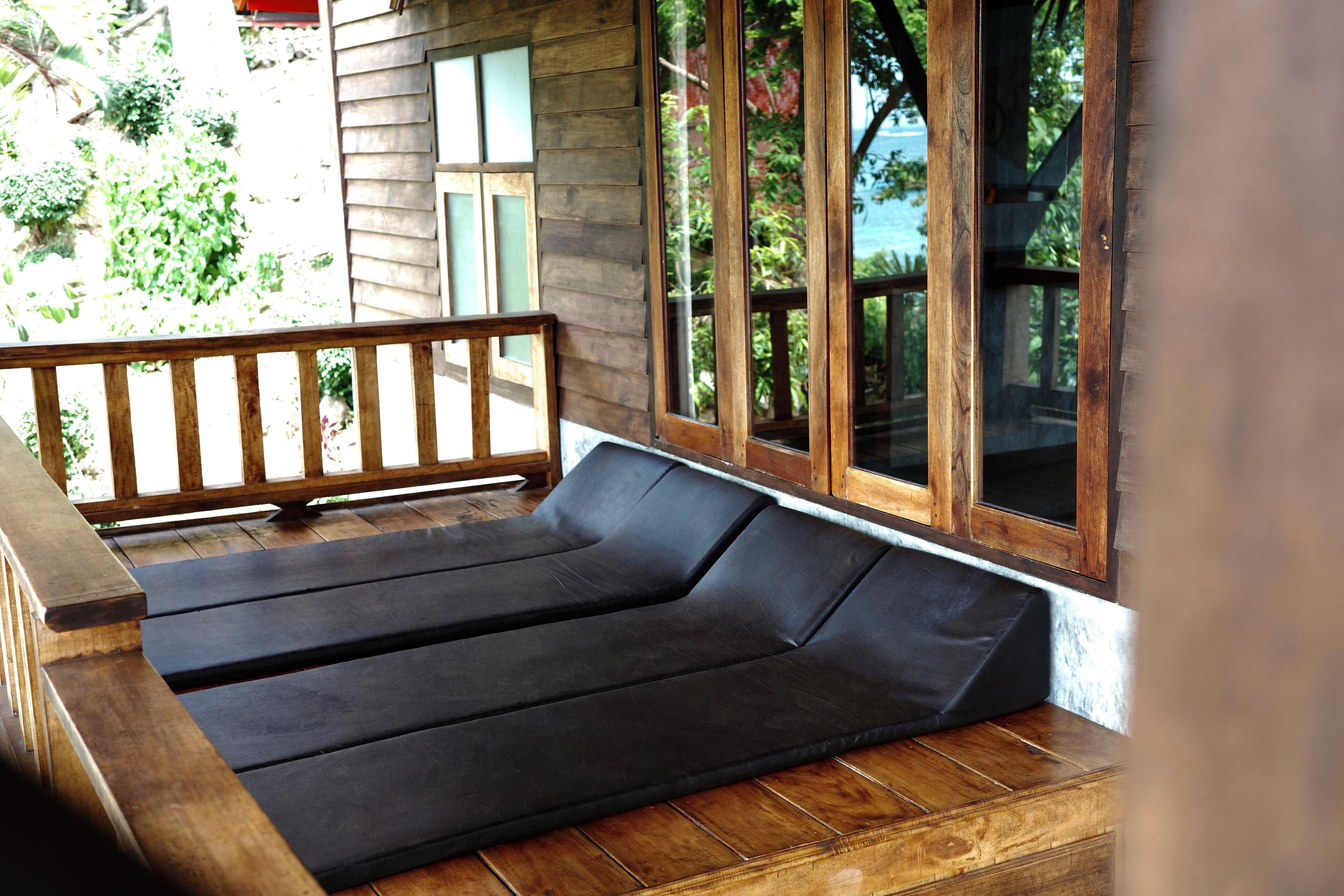 A wooden deck with a black sofa and a wooden railing.