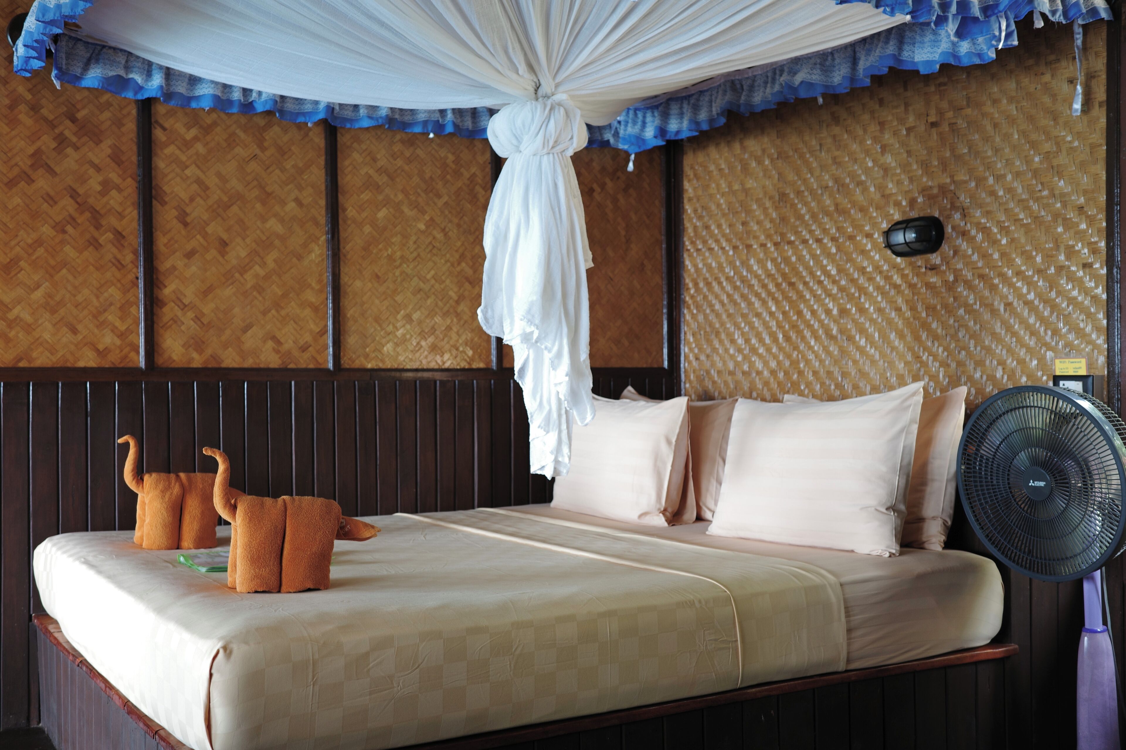 A bed with a canopy, pillows, and a bedside fan.