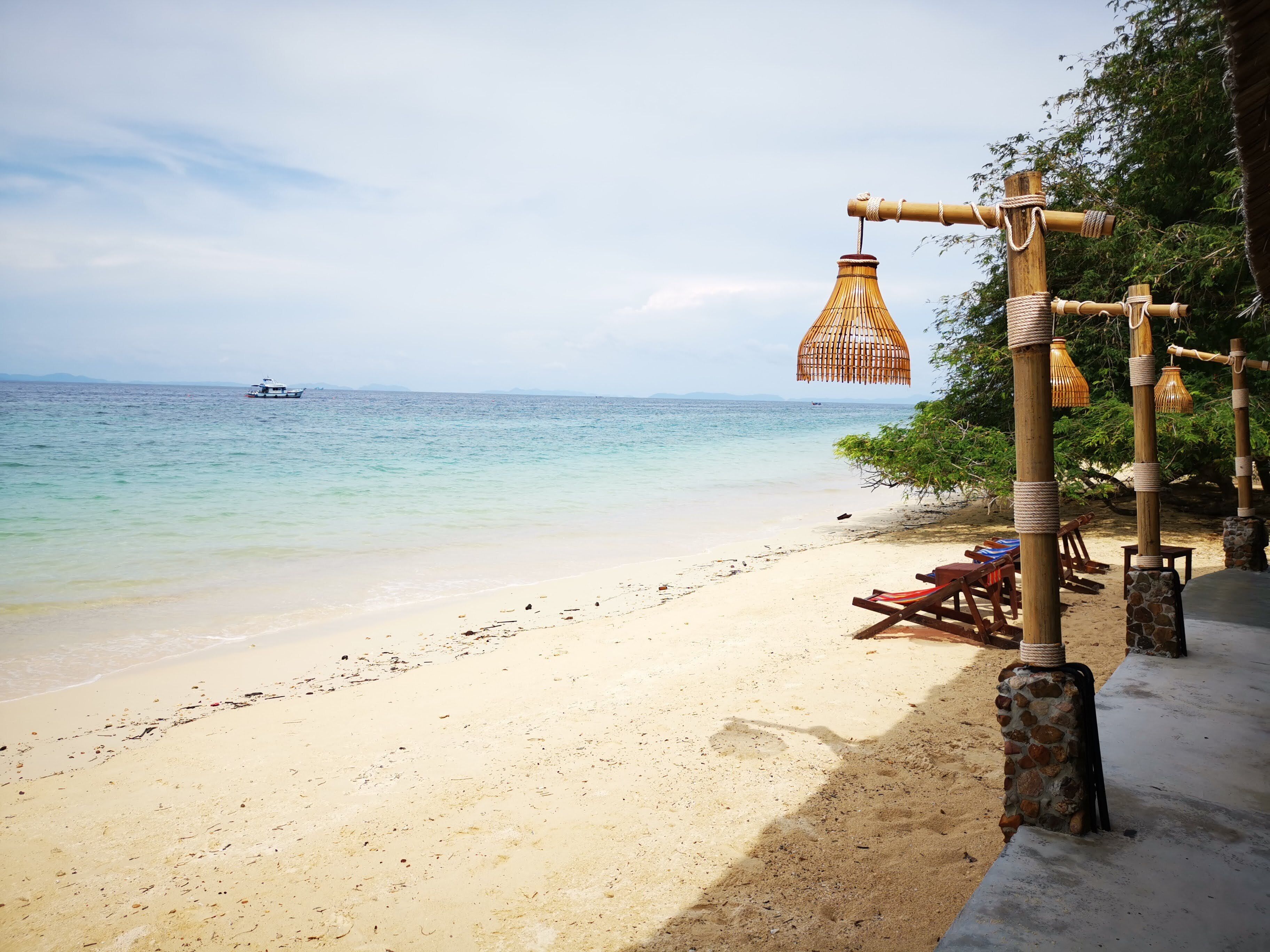 A beach with a wooden structure, a hanging light fixture, and a boat in the distance.