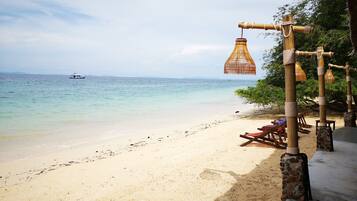 A beach with a wooden structure, a hanging light fixture, and a boat in the distance.