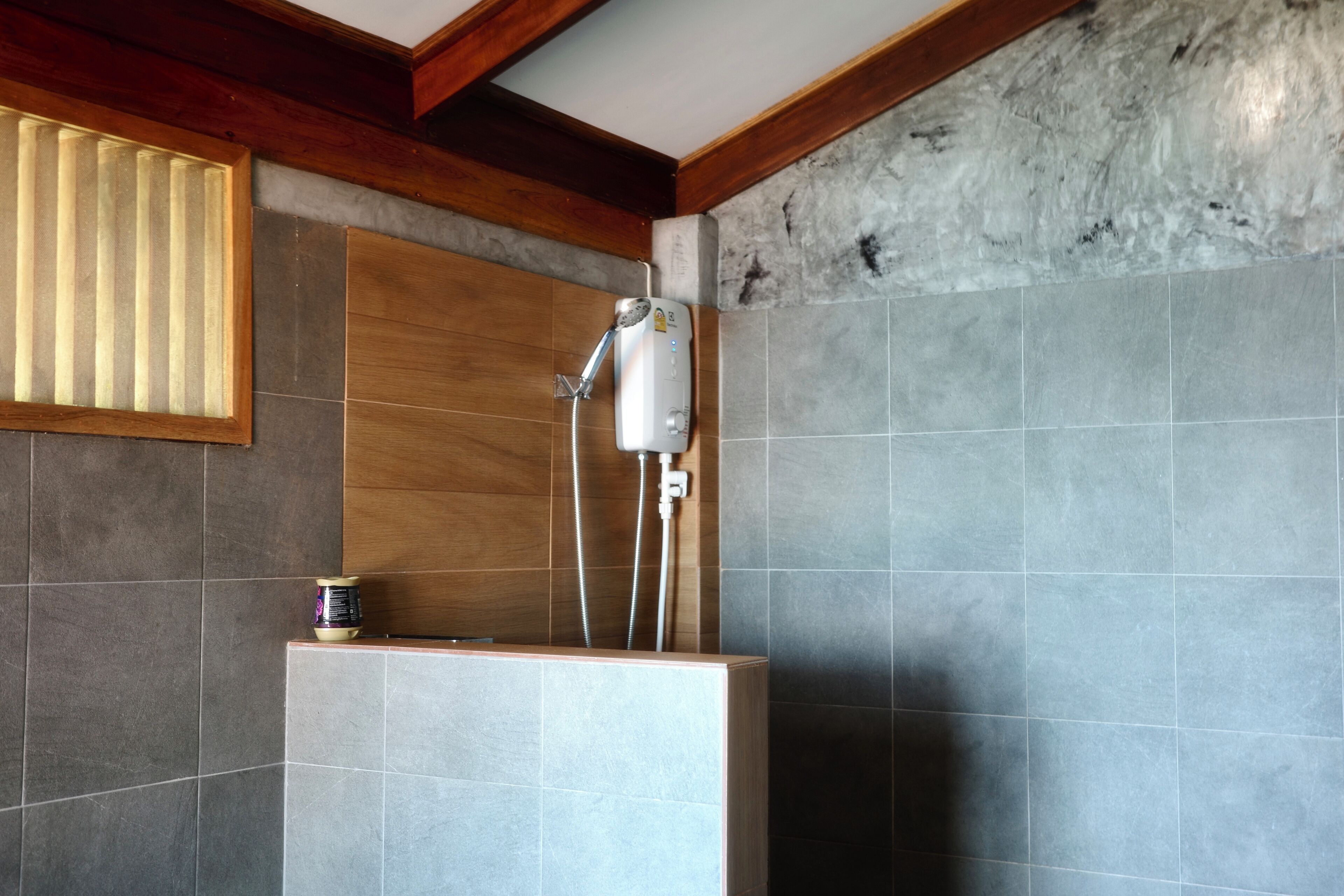 Un baño con ducha, paredes de azulejos y vigas de madera.