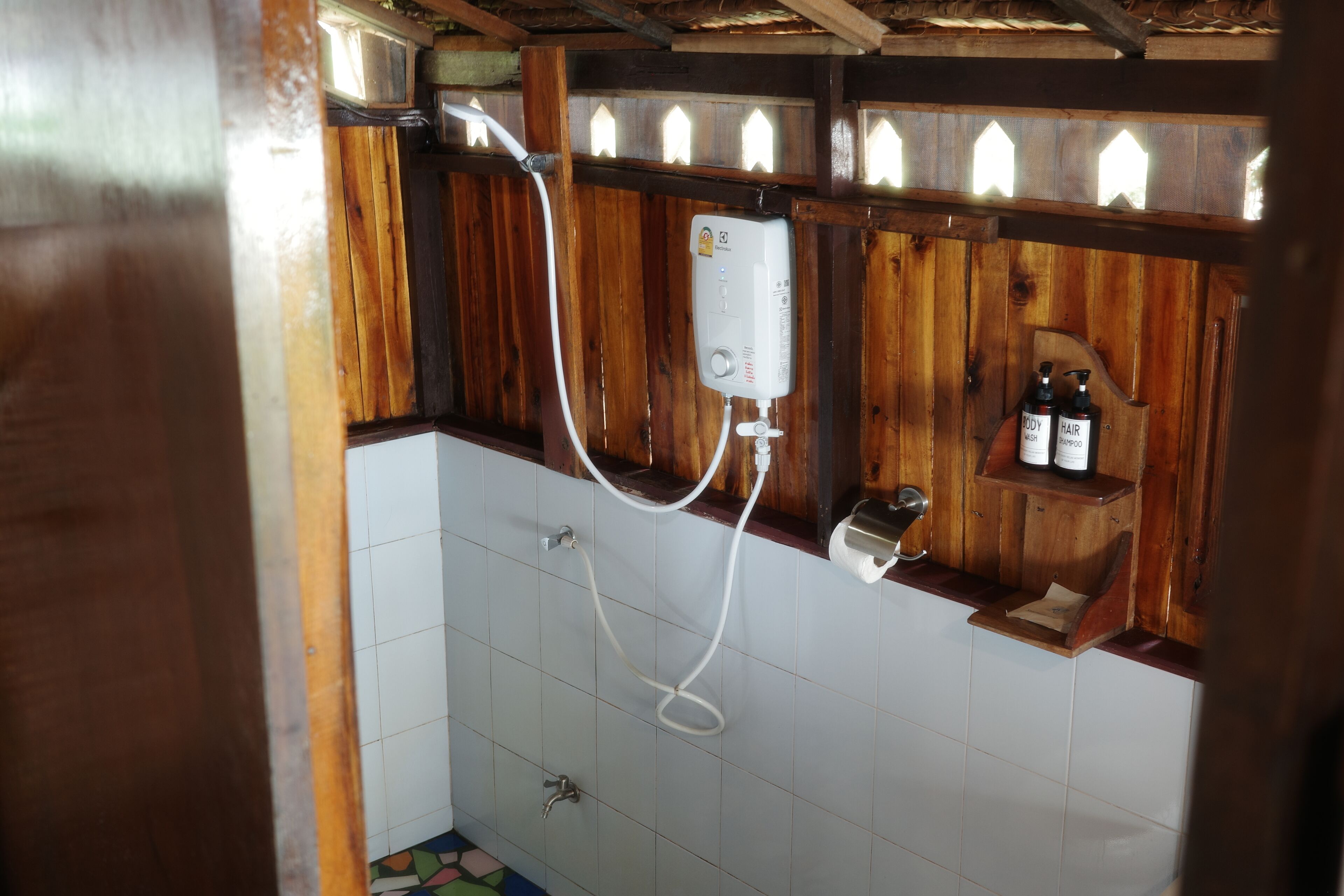 A bathroom with a wooden shower enclosure, a white tiled floor, and a shelf with toiletries.