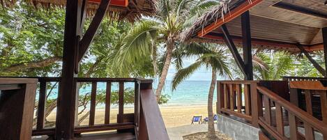 A wooden deck with a view of a beach and palm trees.