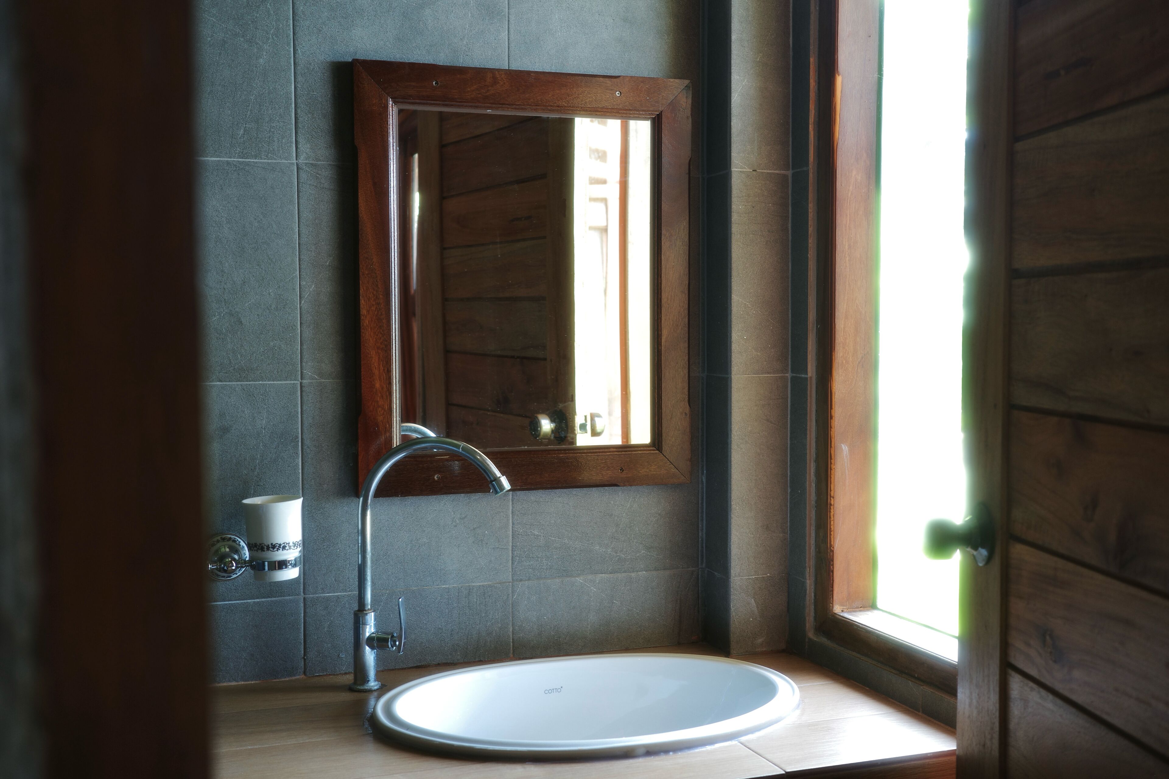 A bathroom with a wooden door, a mirror, a sink, and a window.
