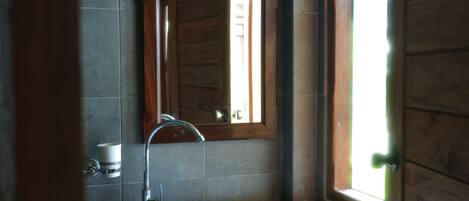 A bathroom with a wooden door, a mirror, a sink, and a window.