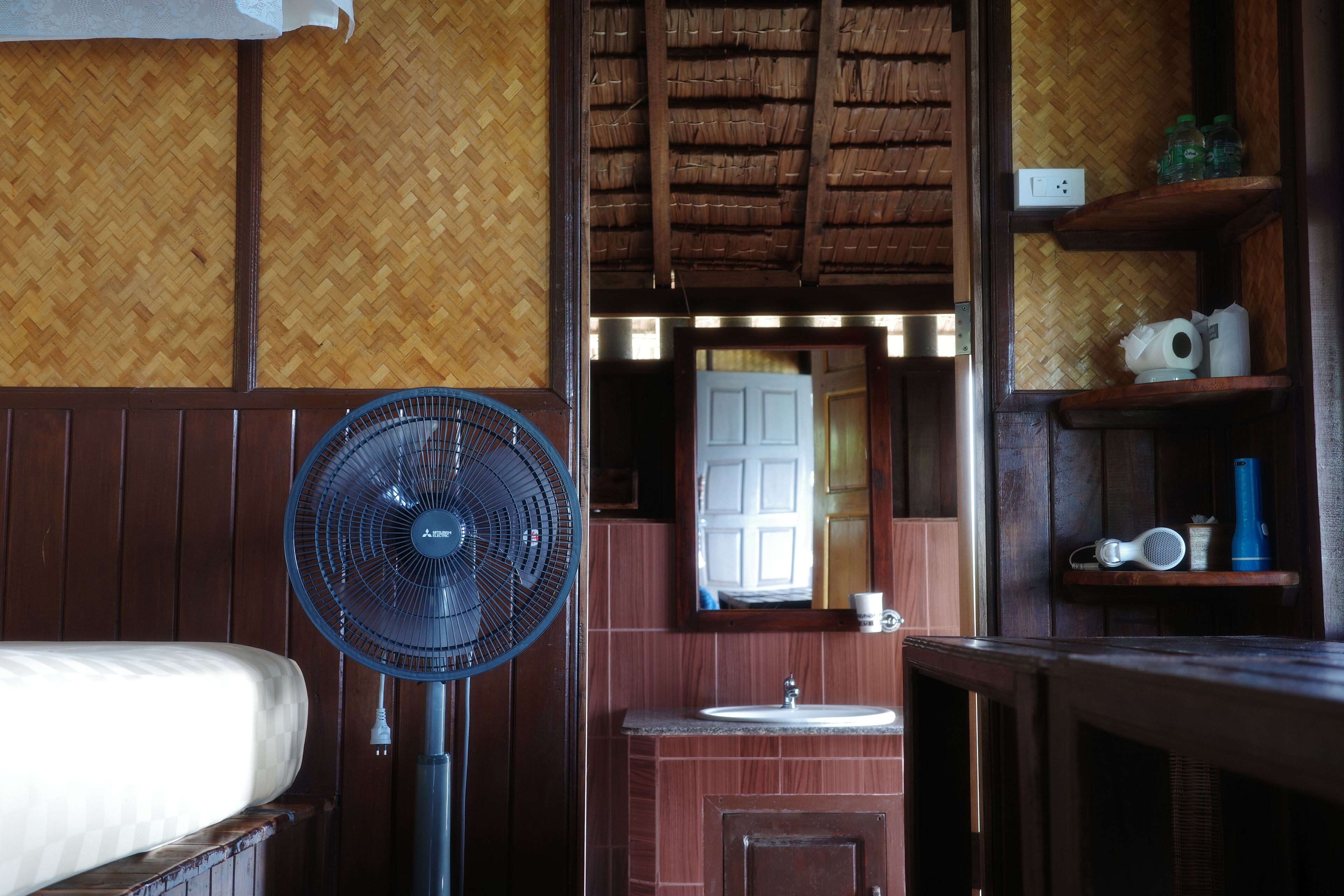 Een kamer met een bed, een ventilator, een wastafel en een spiegel.