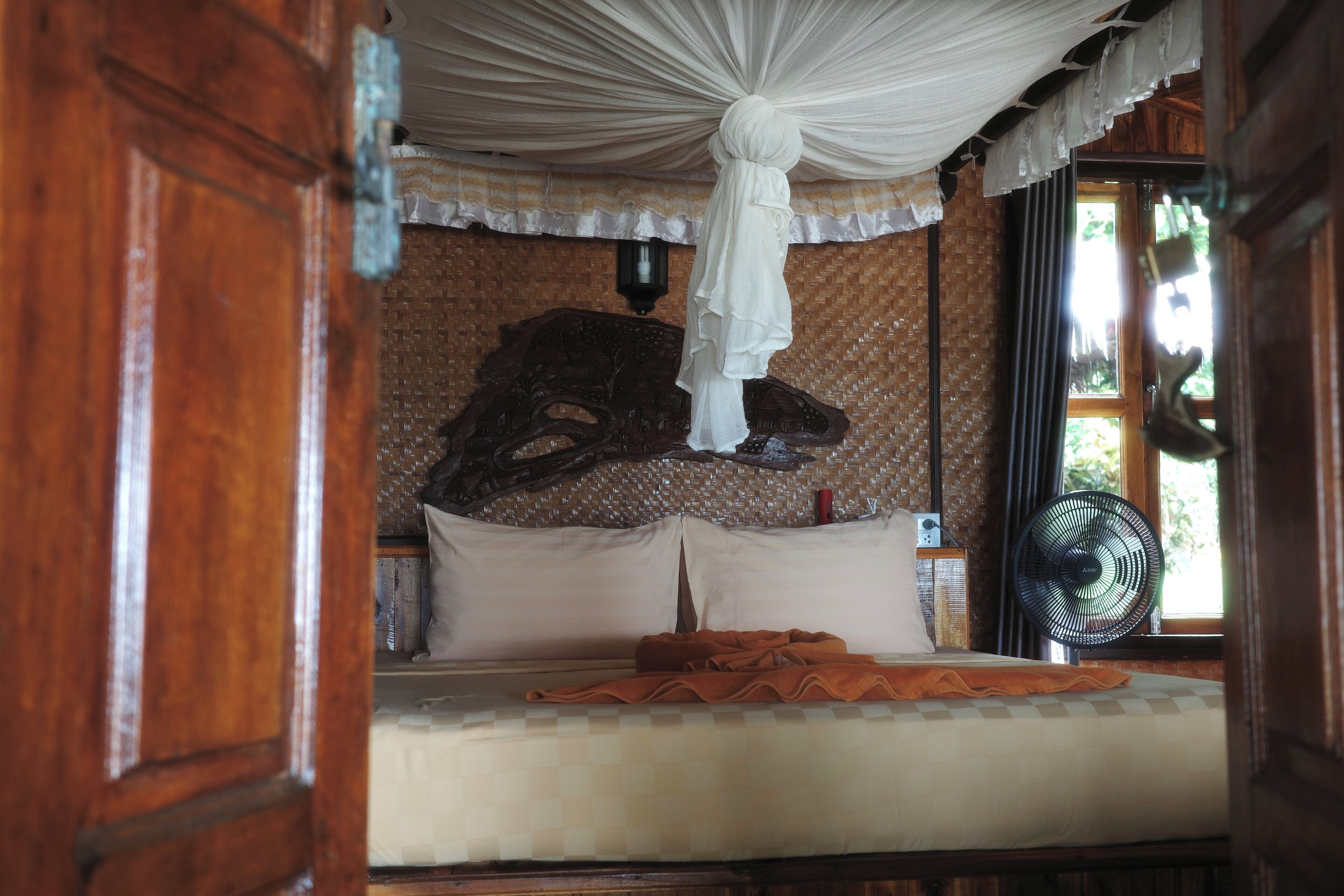 A room with a bed, a hanging canopy, a wall-mounted fan, and a decorative headboard.
