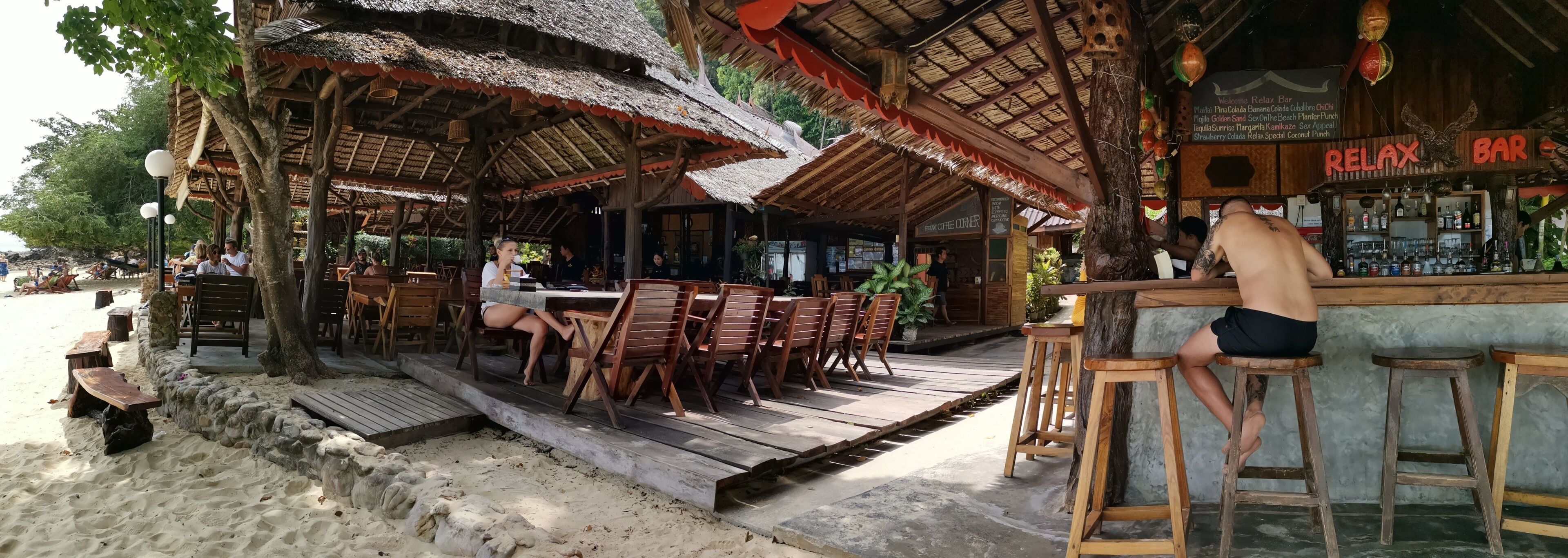 Un bar junto a la playa con mobiliario de madera y techos de paja.