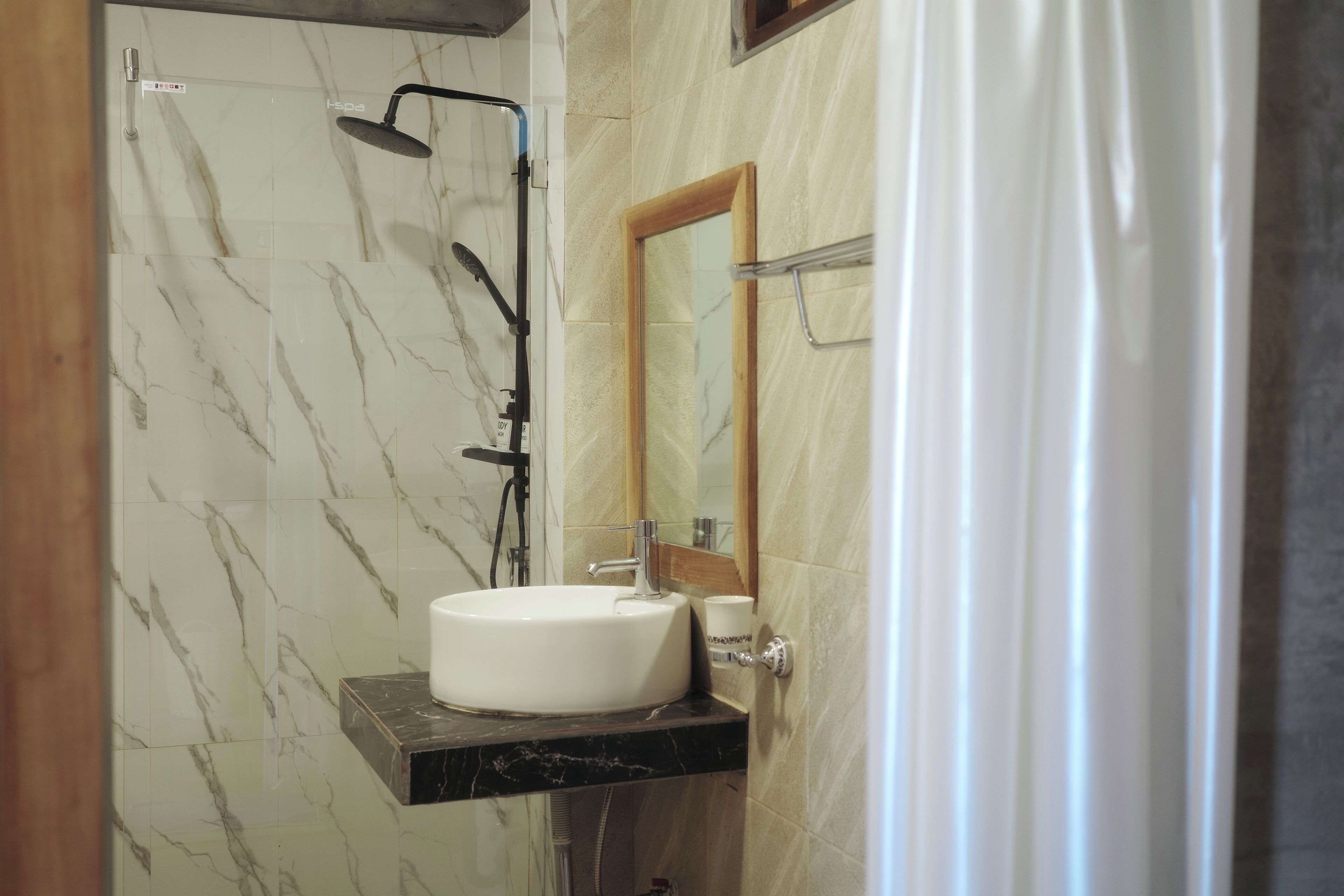 A bathroom with a marble wall, a white sink, and a shower.