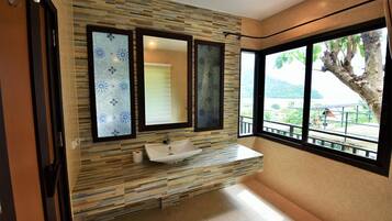 A bathroom with a sink, three mirrors, and a view of a tree and landscape through large windows.