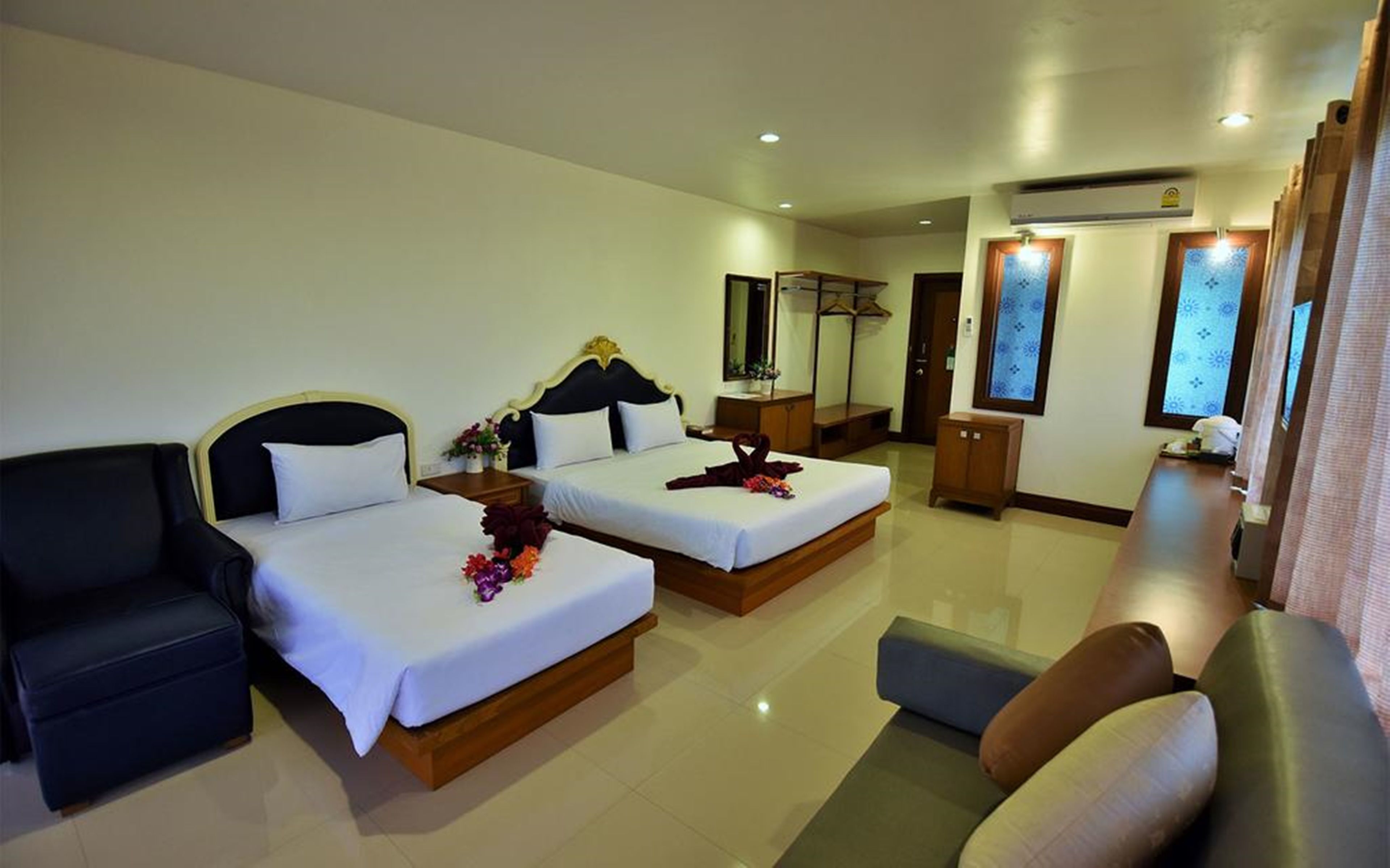 A hotel room with two beds, a sofa, a chair, a small table, and a mirror.