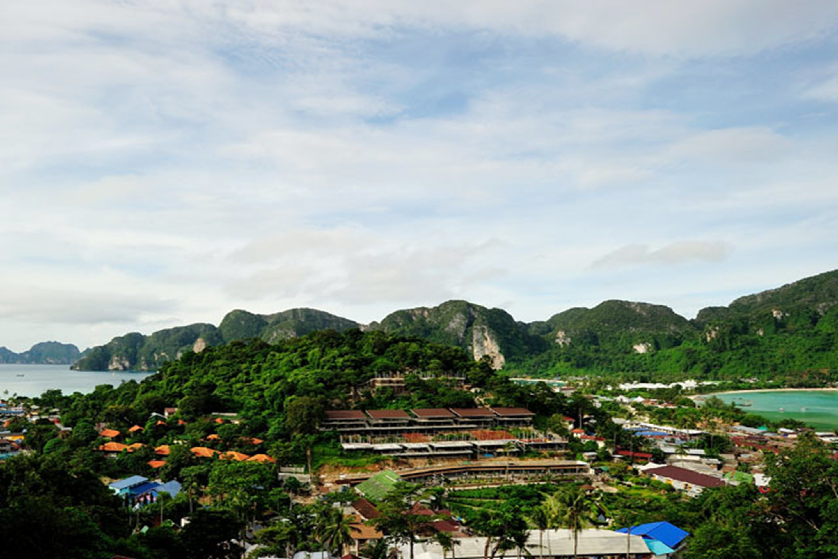 A coastal town with buildings surrounded by lush greenery and mountains.