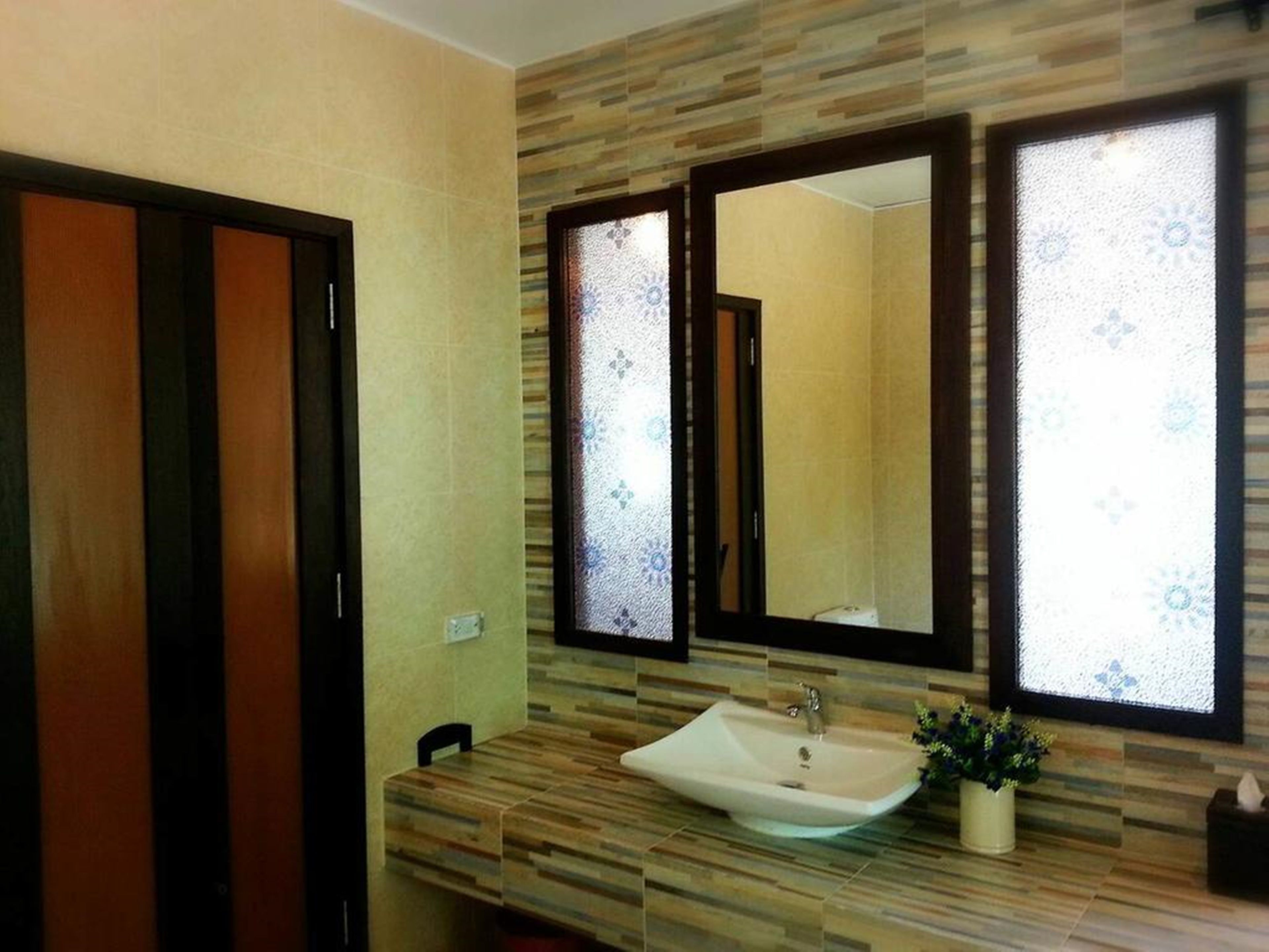 Un baño con tocador de madera, un lavabo y dos espejos con vidrio esmerilado.