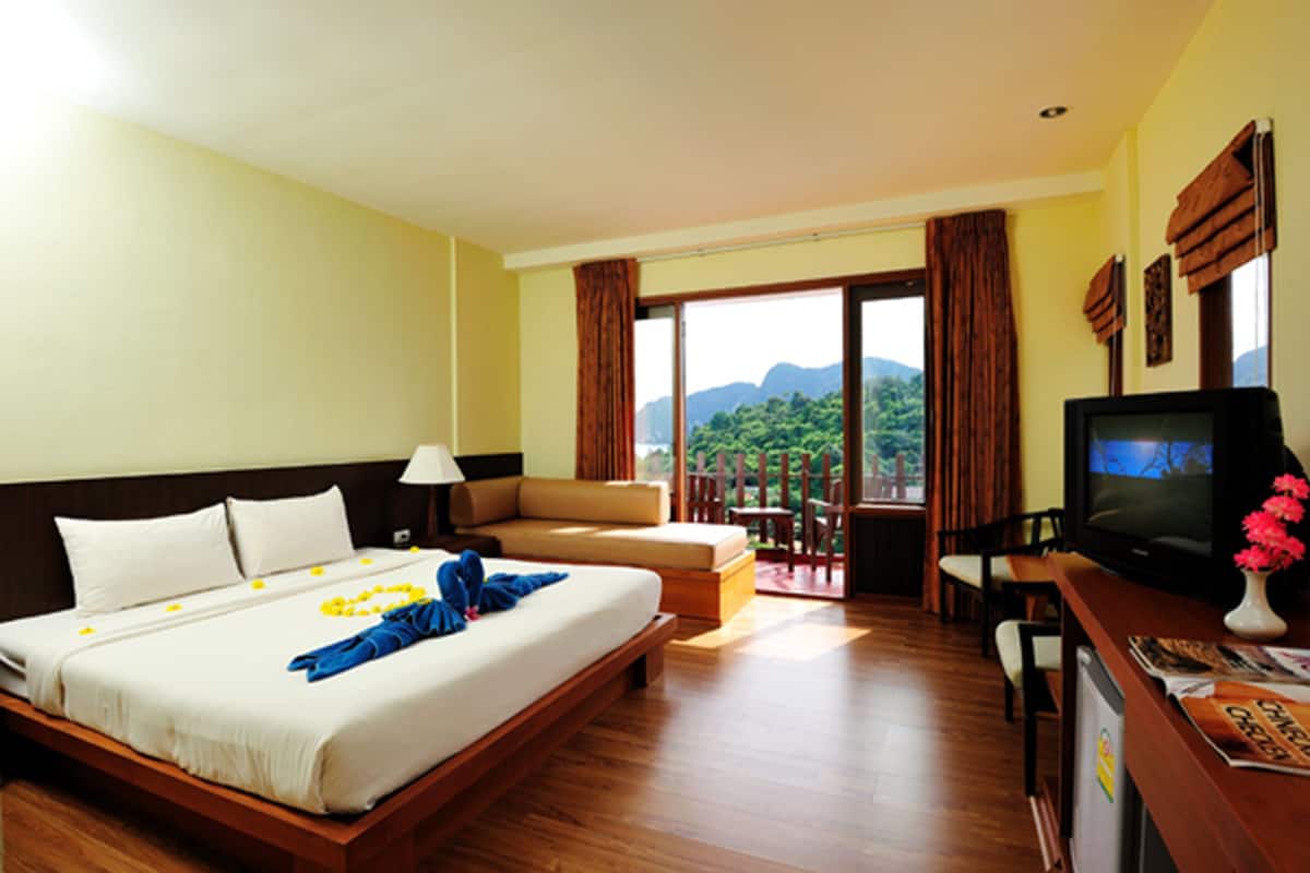 Habitación de hotel con cama, televisor, escritorio y silla, y vista al exterior.