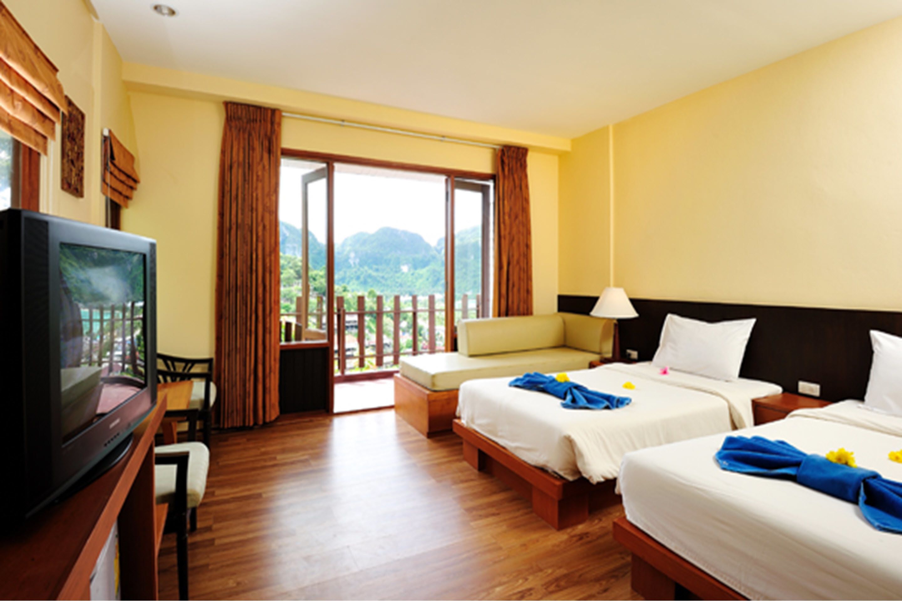 A hotel room with two beds, a television, and a balcony with a view of mountains.